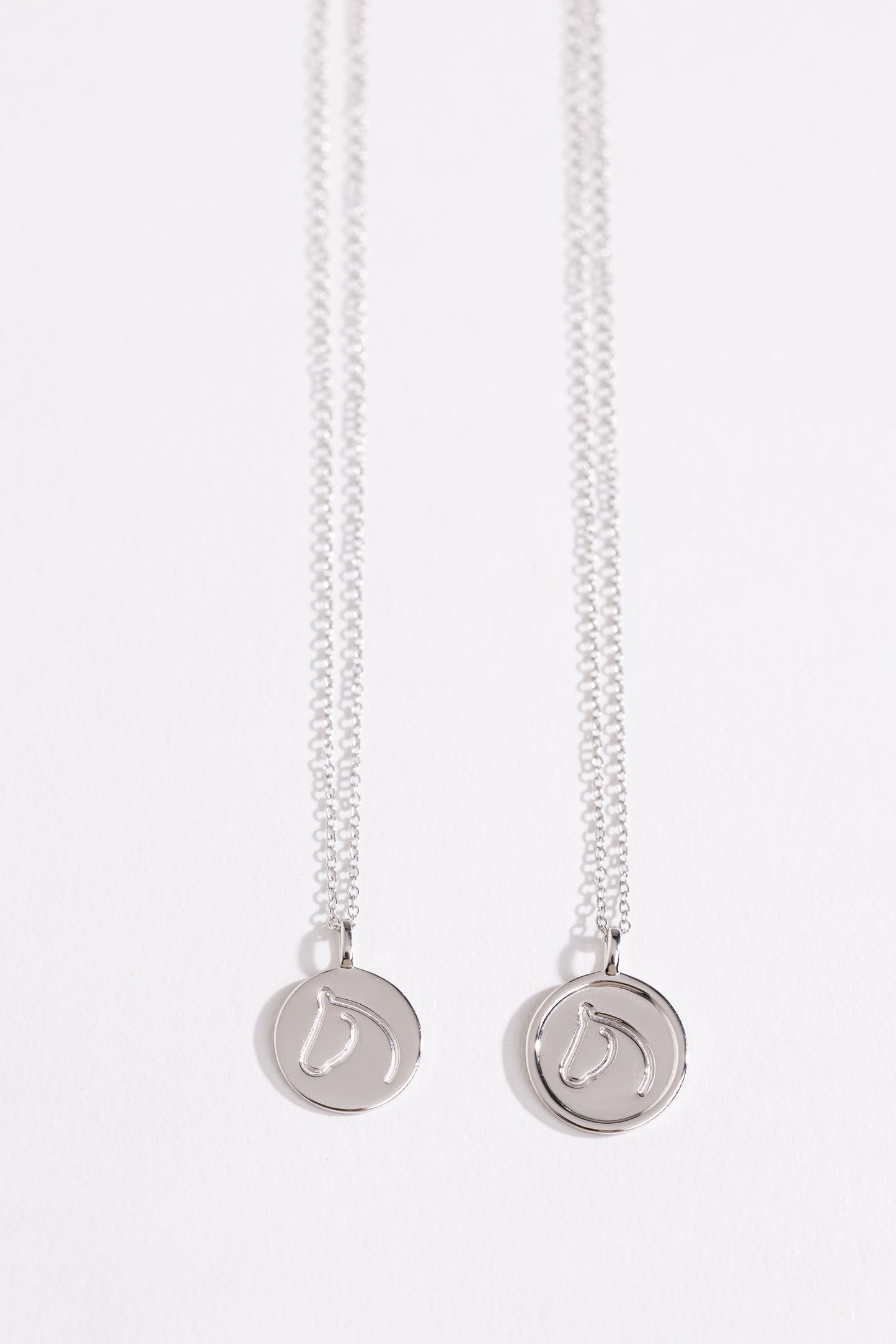 Two Sterling Silver necklaces from The Gilded Horse with round pendants on a white background.