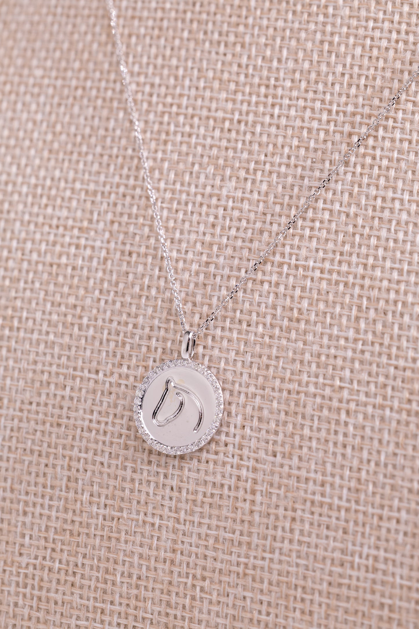 White gold TGH necklace with diamonds on a beige fabric background.
