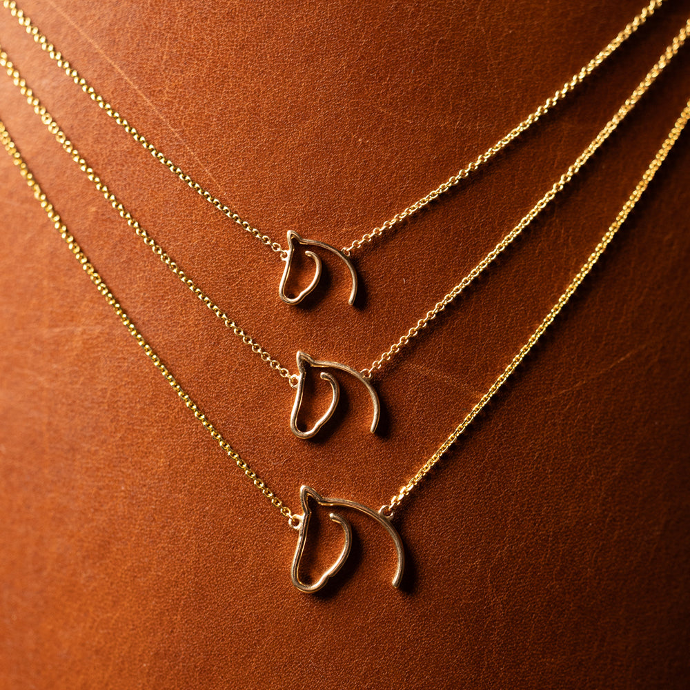 Three gold-tone open horse-head necklaces in graduated lengths on leather