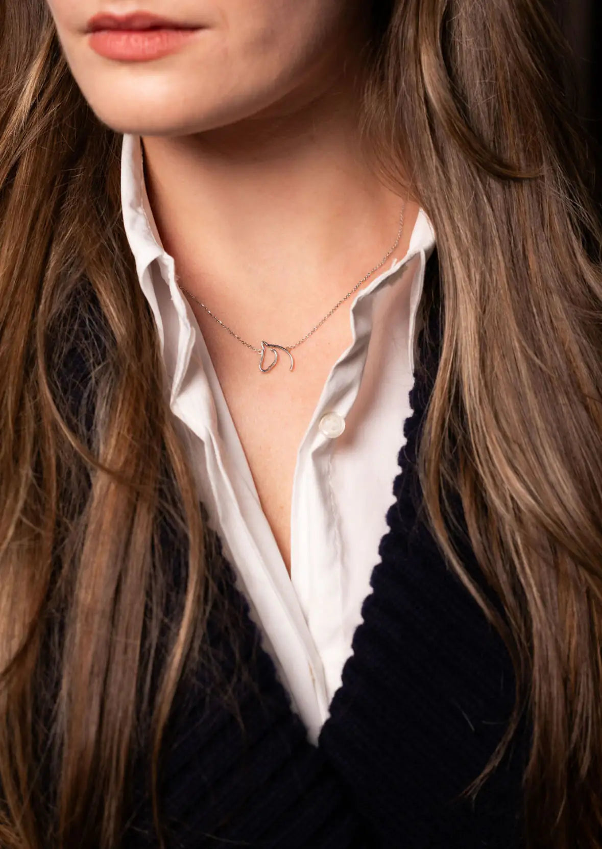 Woman in a white shirt and navy cardigan wearing a silver-tone open horse-head necklace
