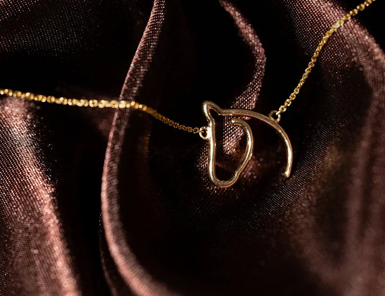Gold-tone open horse-head pendant necklace resting on dark rose fabric