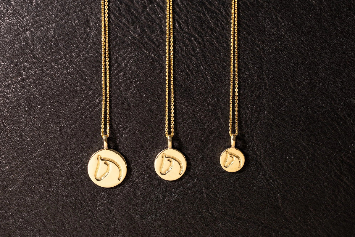 White gold and sterling silver horse necklaces side by side on leather