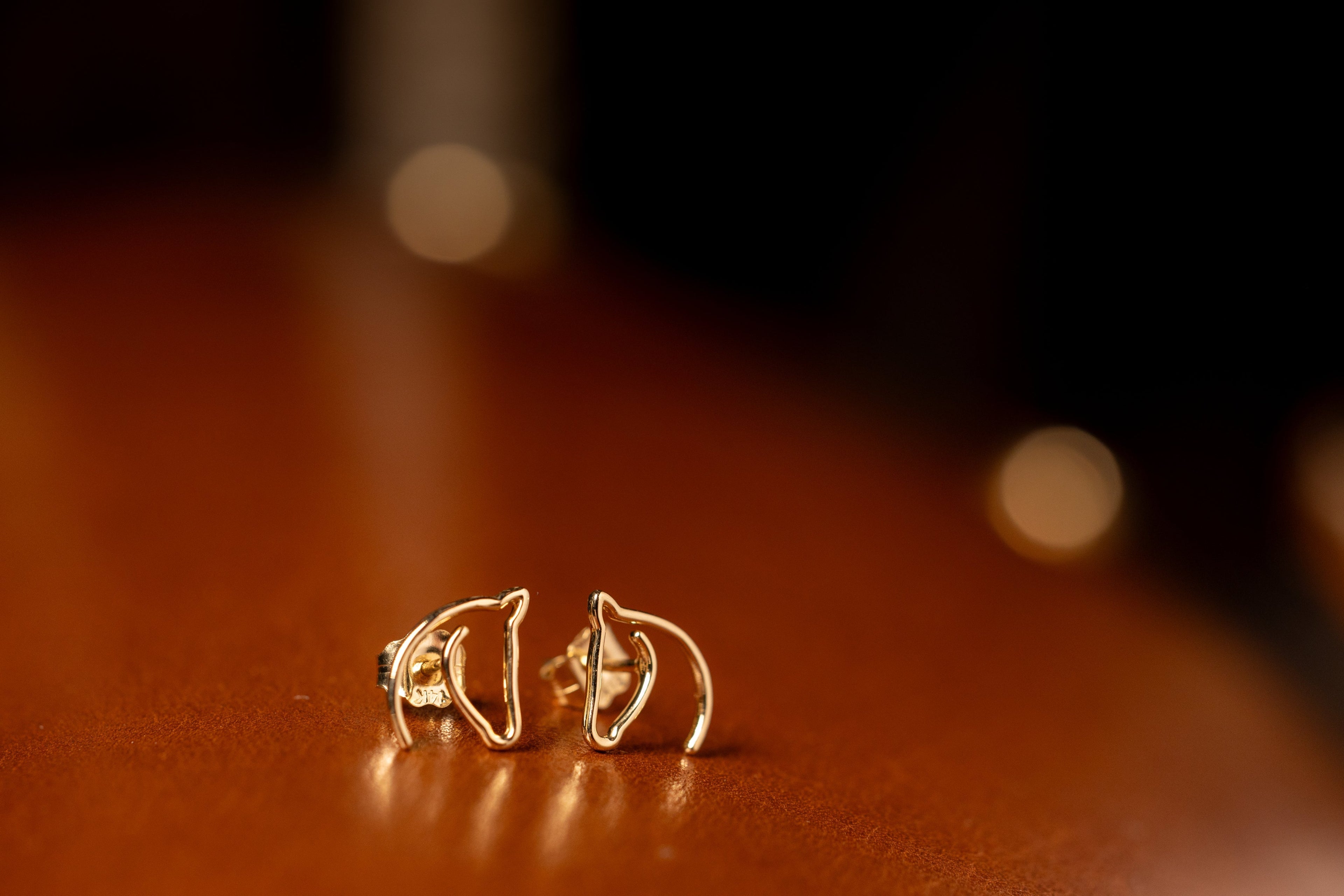 Gold-tone open horse-head stud earrings on a warm leather surface