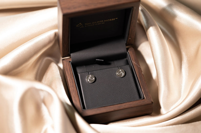 The Gilded Horse silver-tone horse-head stud earrings in a wooden box on champagne satin