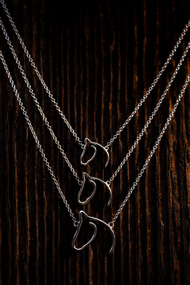 Three layered horse-head pendant necklaces arranged on dark wood