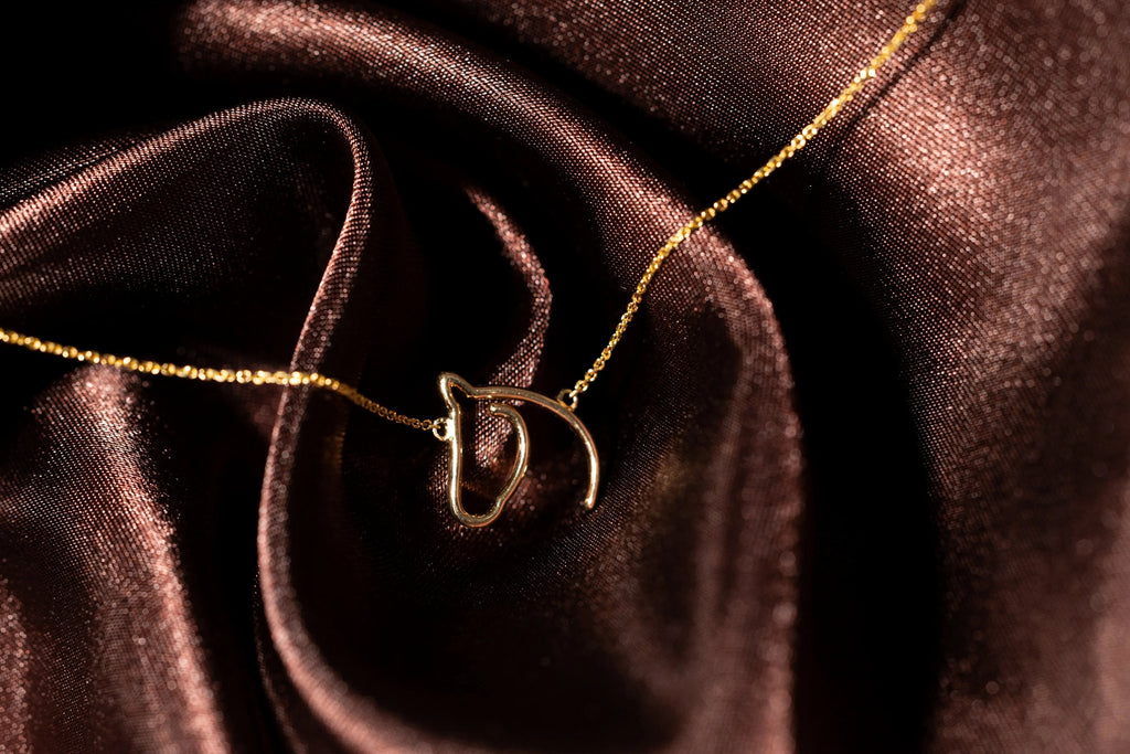 The Gilded Horse solid gold horse-head pendant on a fine chain over dark wood