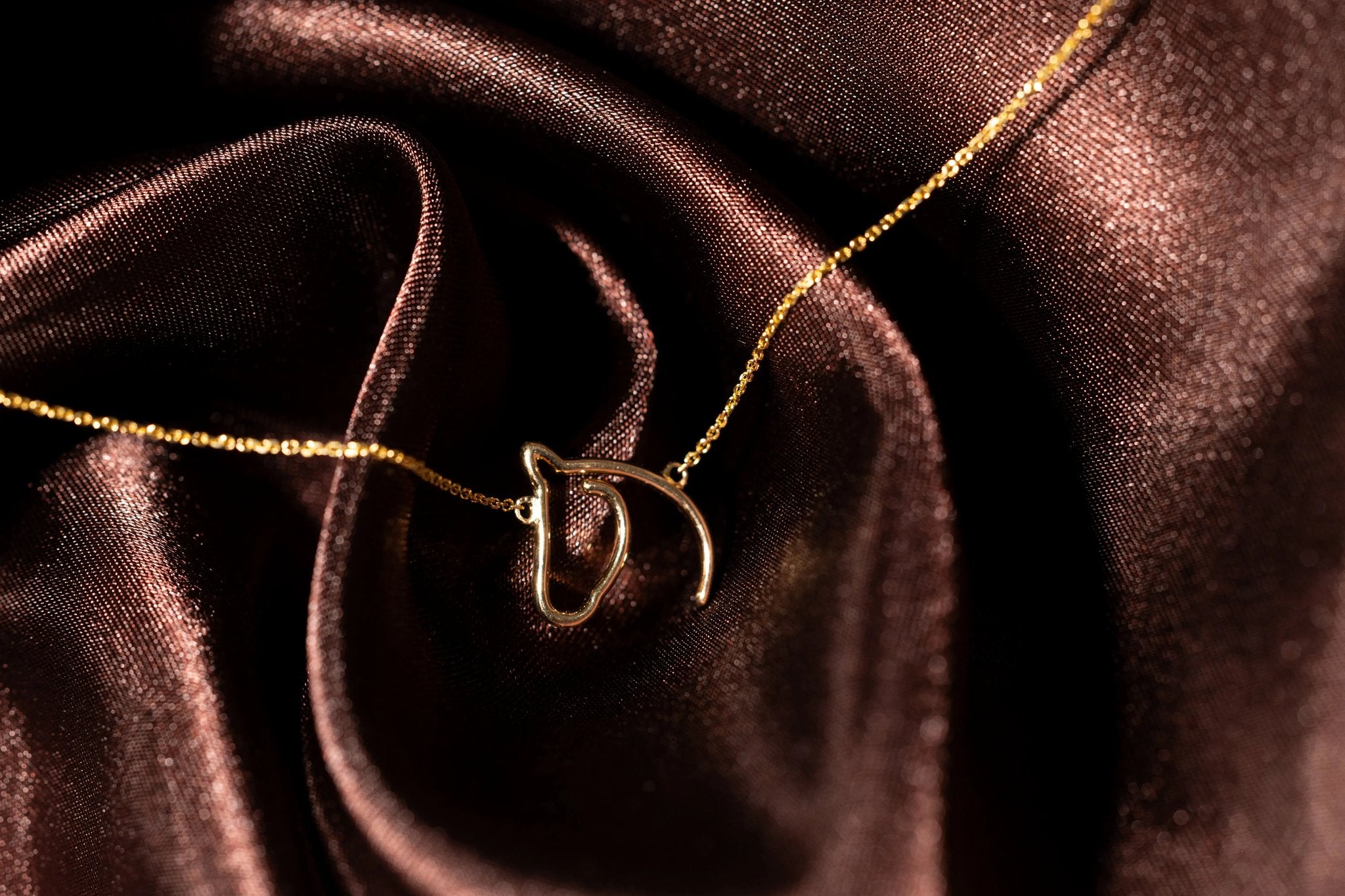 The Gilded Horse solid gold horse-head pendant on a fine chain over dark wood