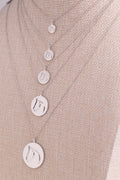 Five White Gold Circle Medallion Pendant Necklaces from The Gilded Horse (Small, Medium, Large, XL & XXL), on a beige mannequin.  
