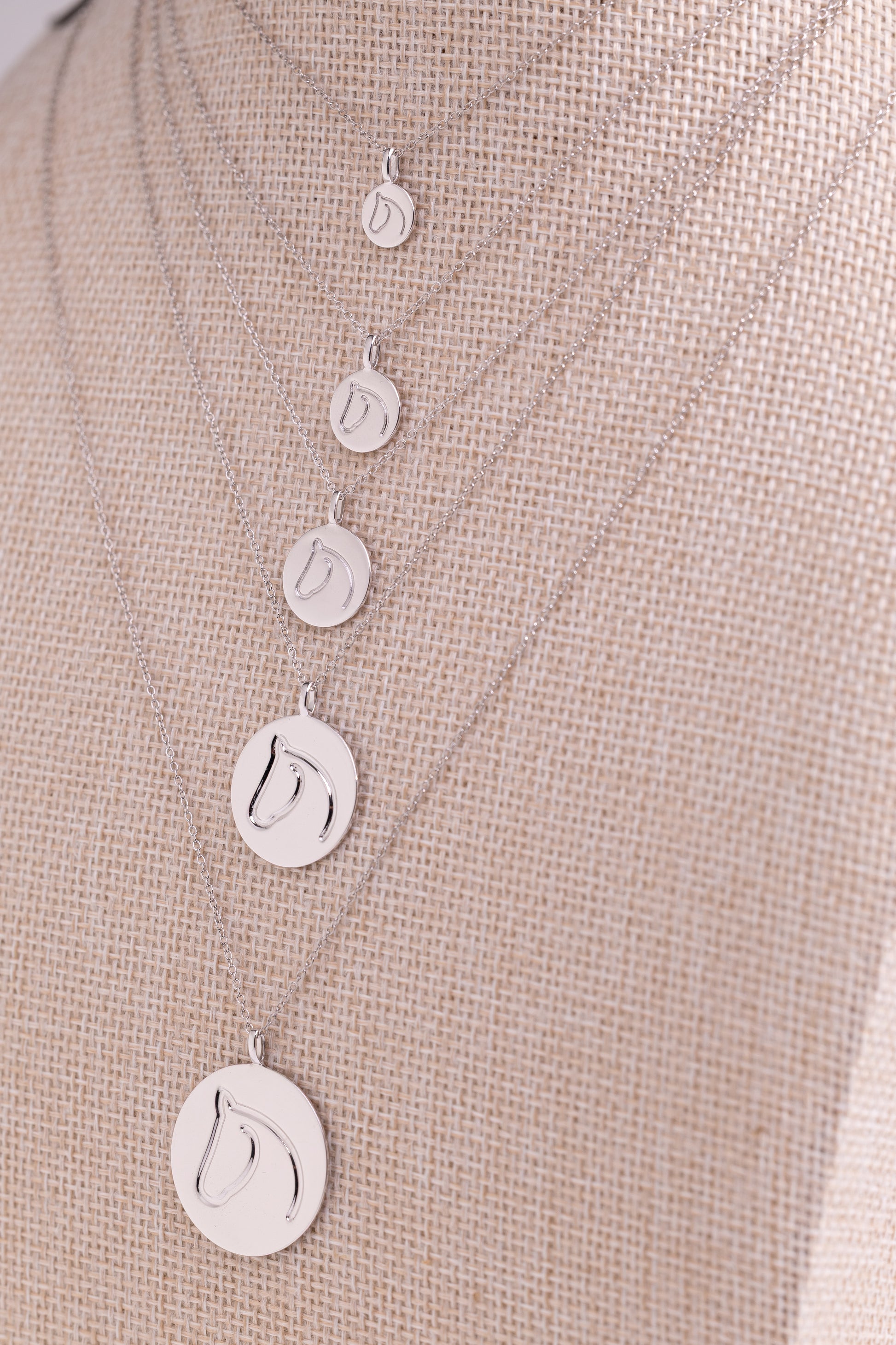 Five White Gold Circle Medallion Pendant Necklaces from The Gilded Horse (Small, Medium, Large, XL & XXL), on a beige mannequin.  