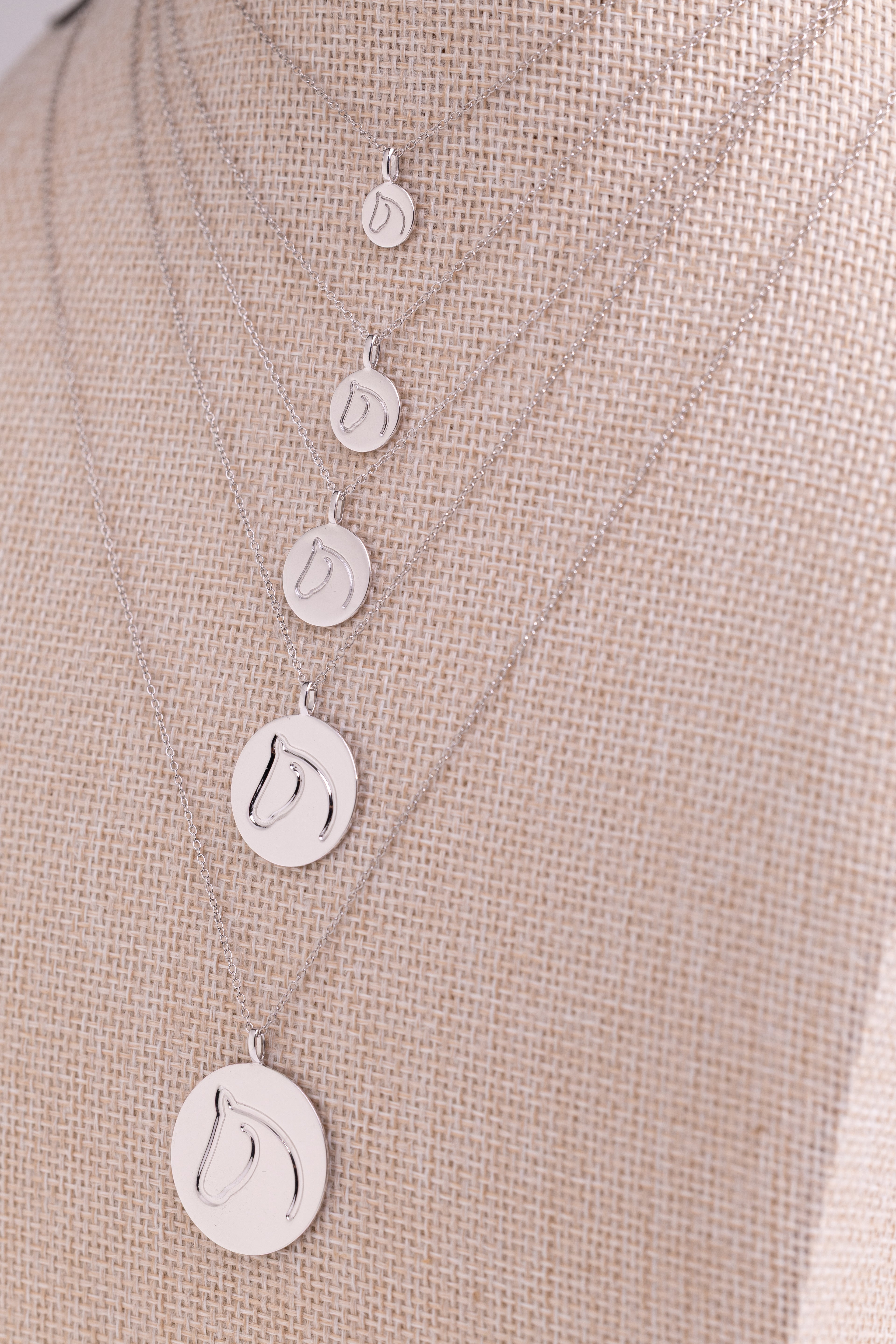 Five White Gold Circle Medallion Pendant Necklaces from The Gilded Horse (Small, Medium, Large, XL & XXL), on a beige mannequin.  