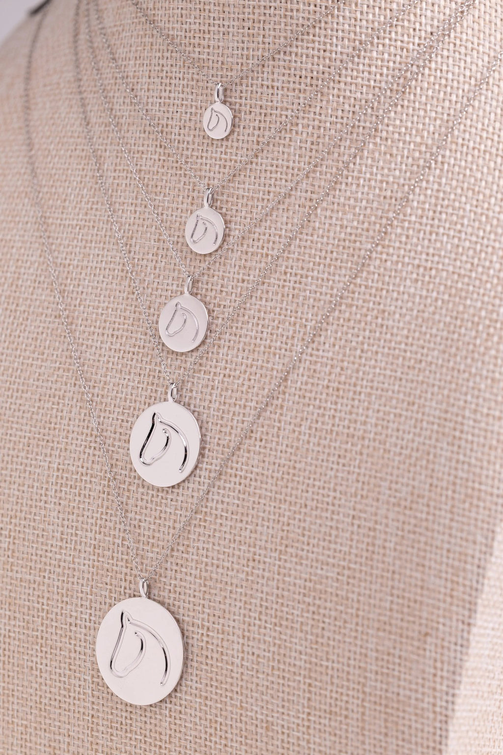 Five sterling silver circle medallion horse necklaces in graduated sizes on a beige bust