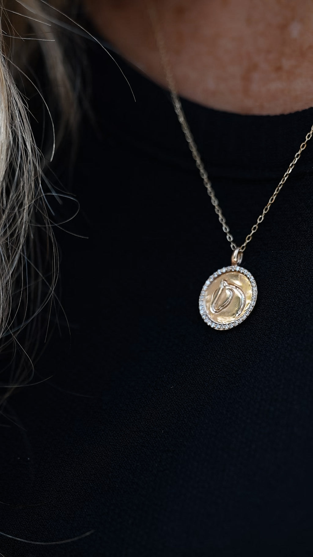 Gold horse medallion necklace with diamond border worn over a black top