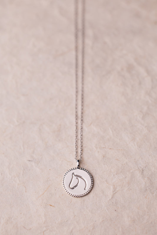 Silver necklace with a round horse pendant on a beige background.