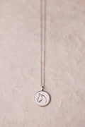 Silver necklace with a round horse pendant on a beige background.