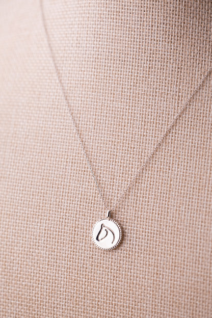 Silver necklace with a round horse pendant on a beige fabric background.
