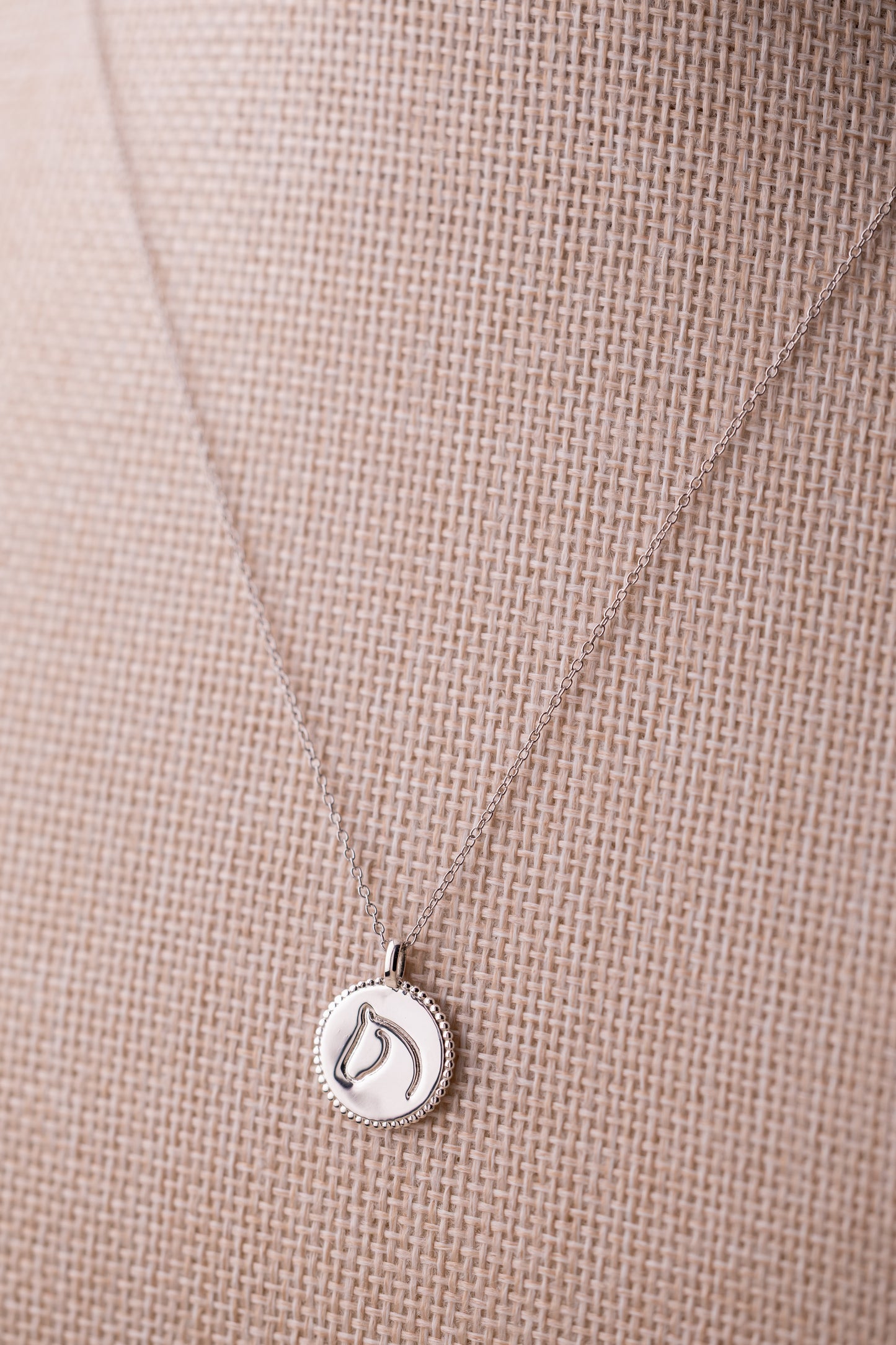 Silver necklace with a horse pendant on a beige fabric background.