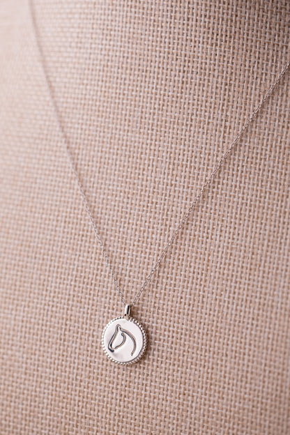 Silver necklace with a horse pendant on a beige fabric background.