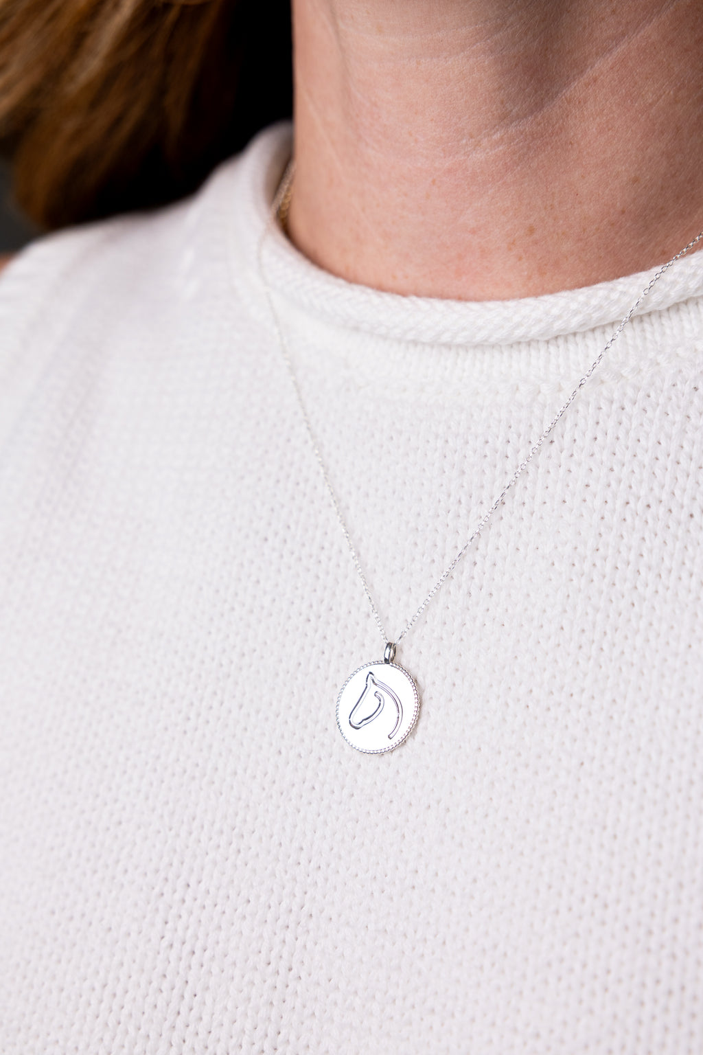 Silver necklace with a pendant worn by a person on a light background