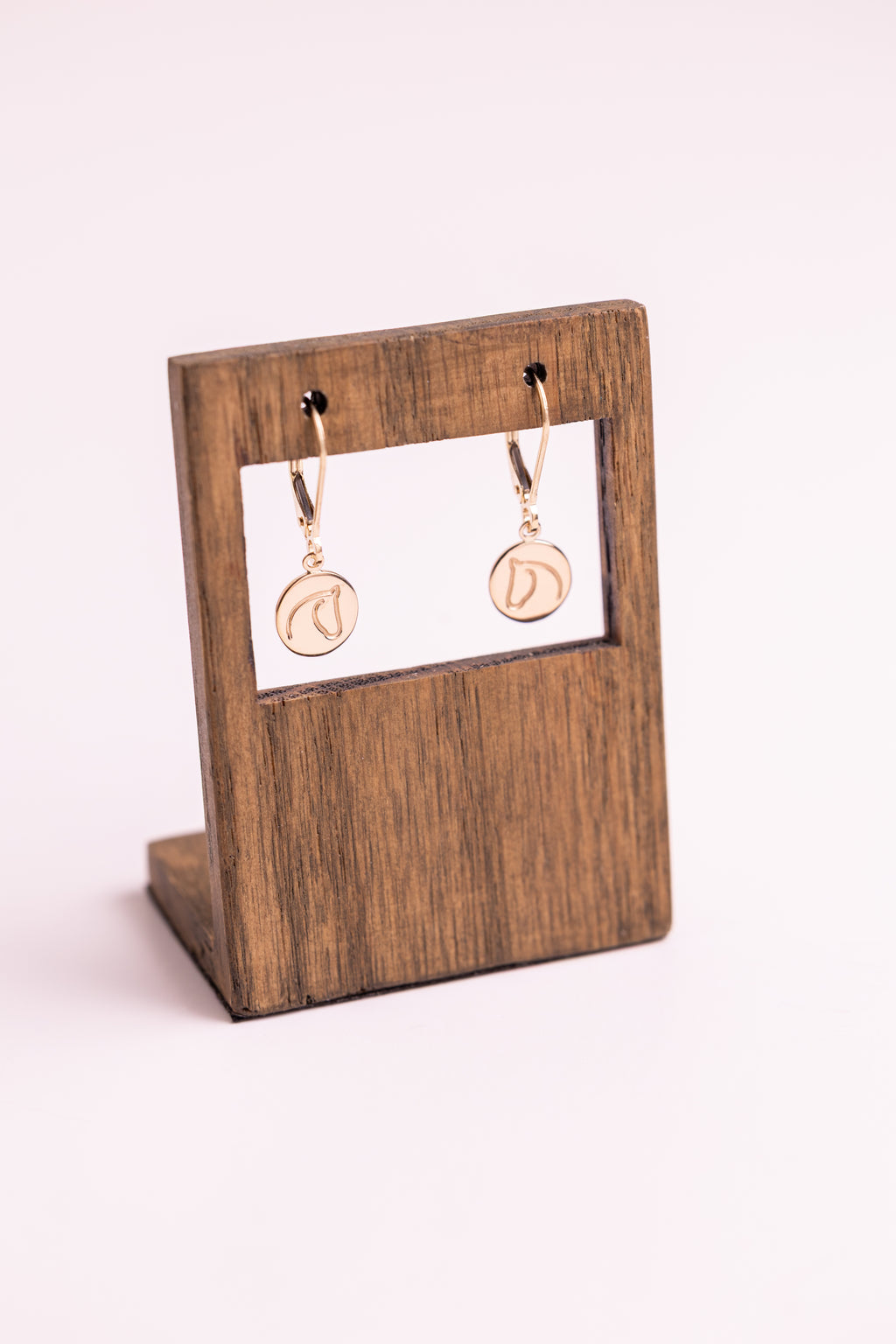 Gold earrings with The Gilded Horse logo on a wooden display stand with a white background.