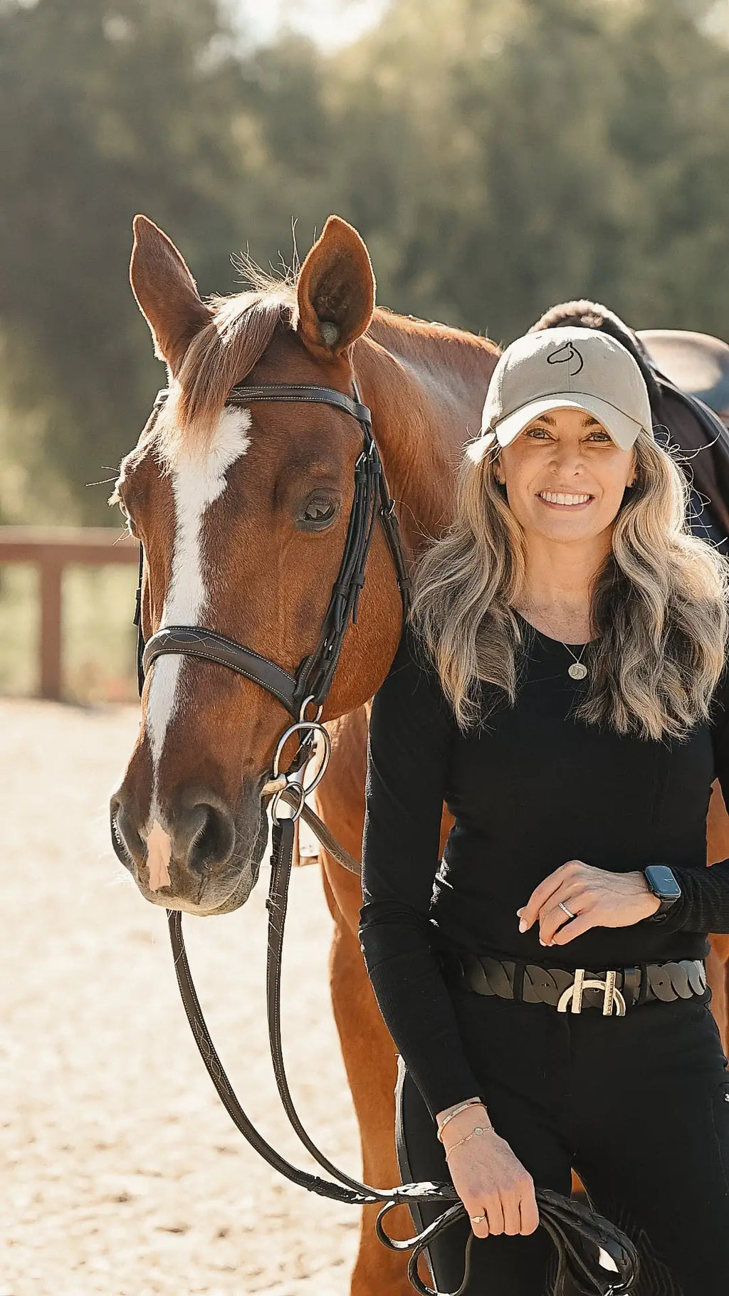 Smiling woman standing beside a chestnut horse, wearing The Gilded Horse khaki embroidered cap