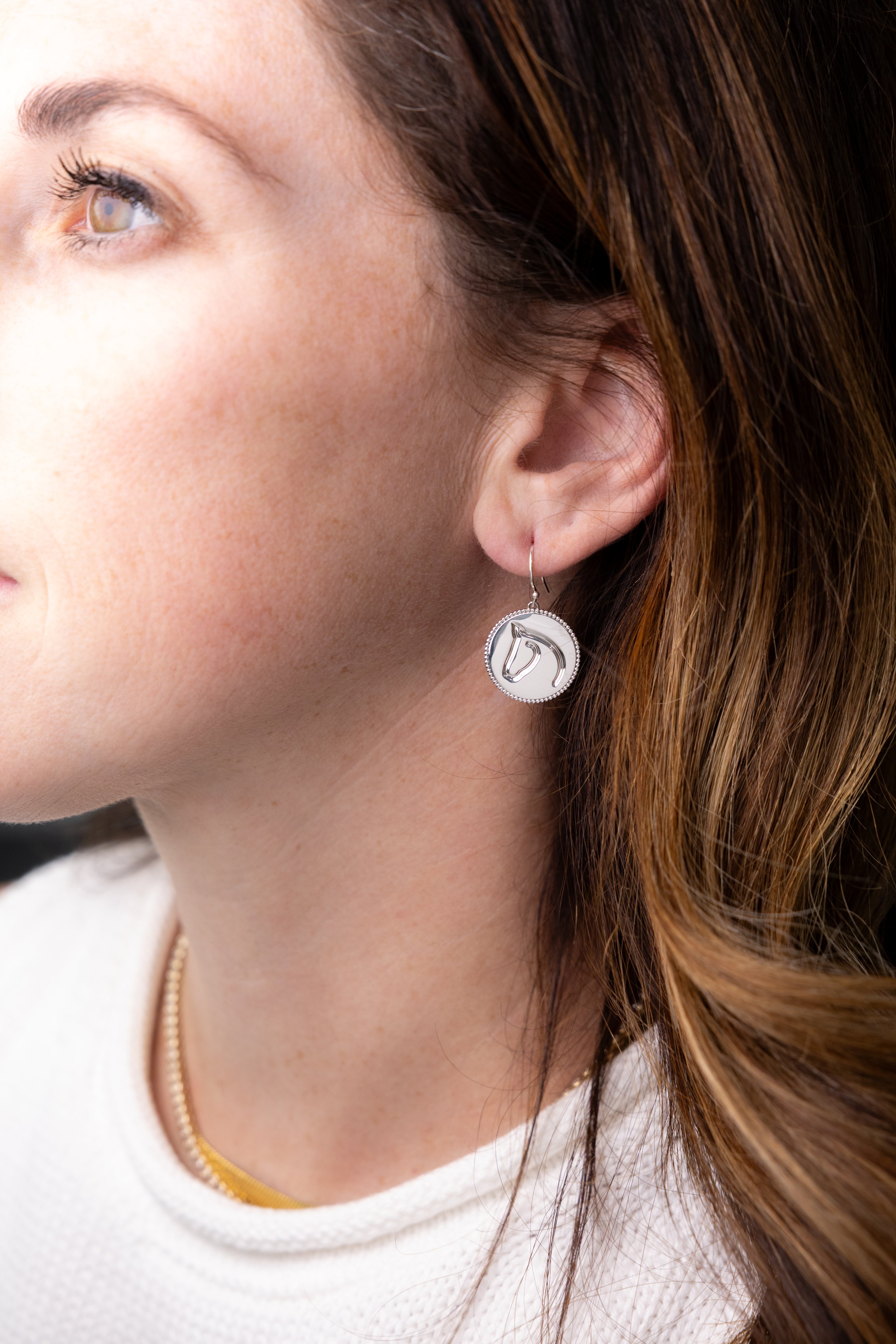 Close-up of a person wearing a silver earring with a circular design.
