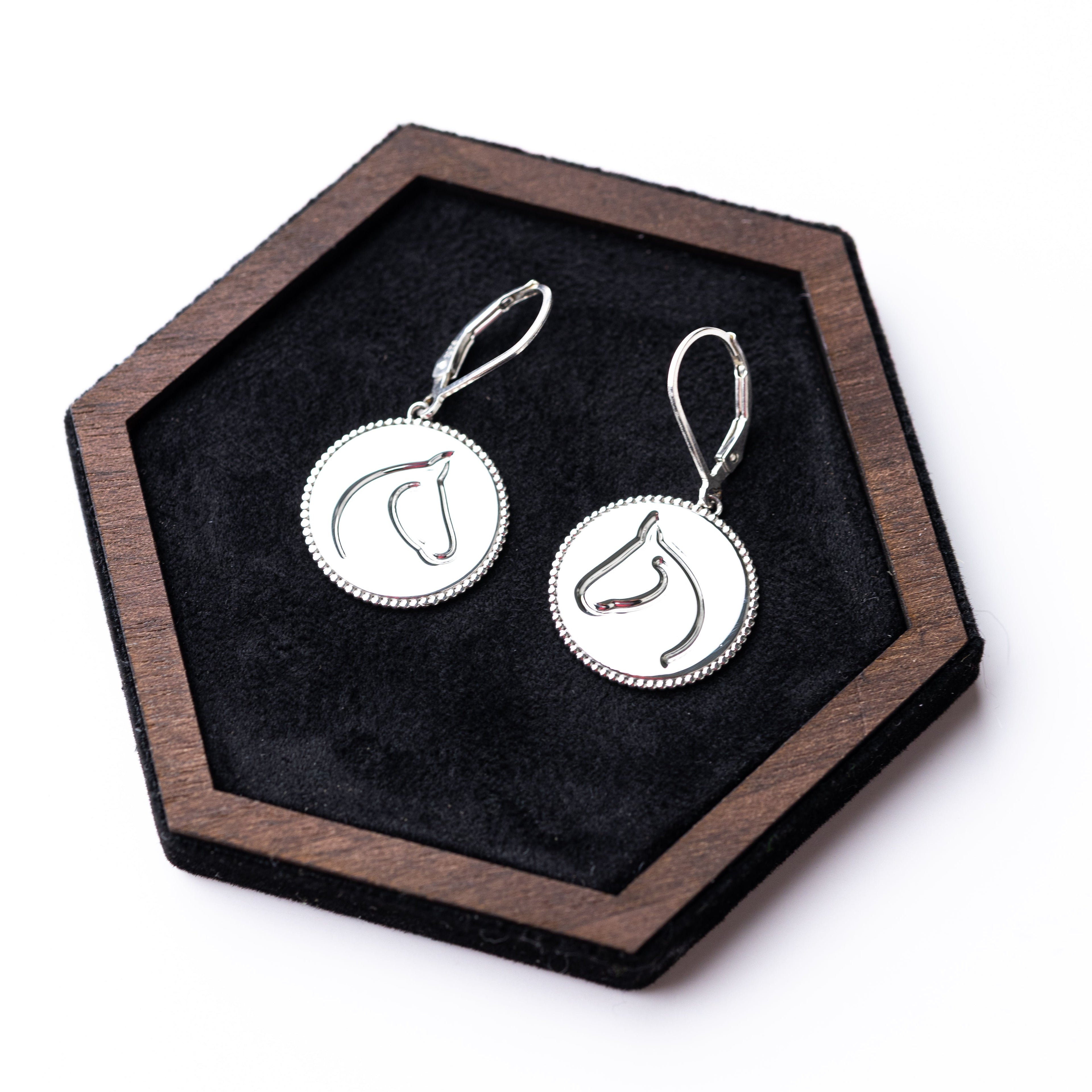 Silver earrings on a hexagonal wooden stand with black felt