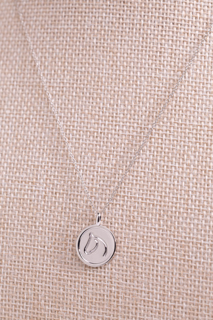 Sterling silver necklace with a round pendant from The Gilded Horse, on a beige fabric background.