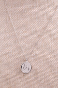 Sterling silver necklace with a round pendant from The Gilded Horse, on a beige fabric background.