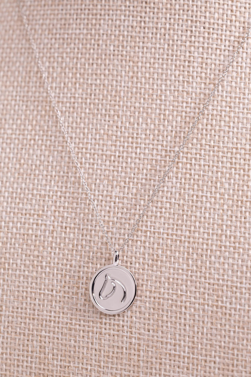 Sterling silver circle medallion horse necklace draped on beige woven fabric