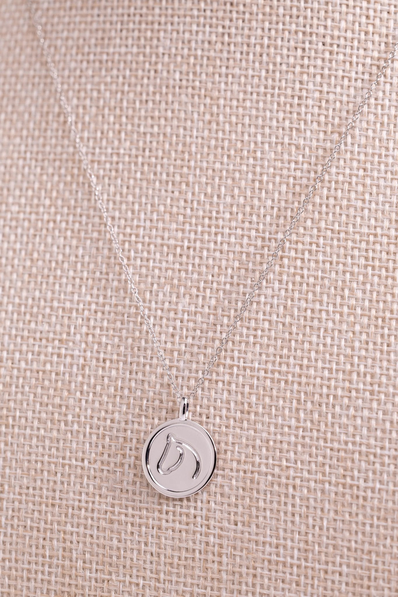 Sterling silver circle medallion horse necklace draped on beige woven fabric