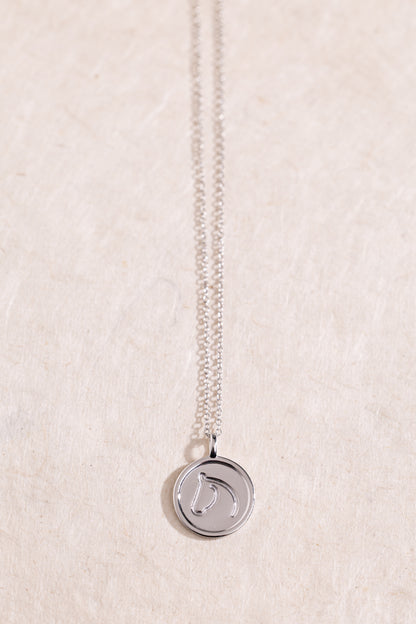 Sterling Silver necklace from The Gilded Horse with a round pendant, on a textured beige background.