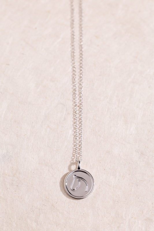 Sterling Silver necklace from The Gilded Horse with a round pendant, on a textured beige background.