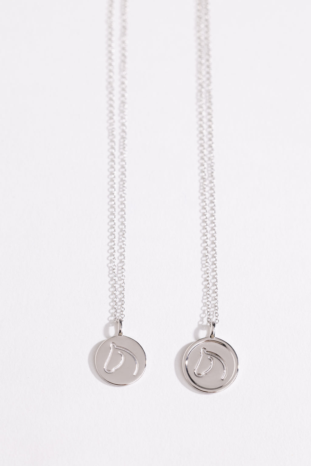 Two Sterling Silver necklaces from The Gilded Horse with round pendants on a white background.