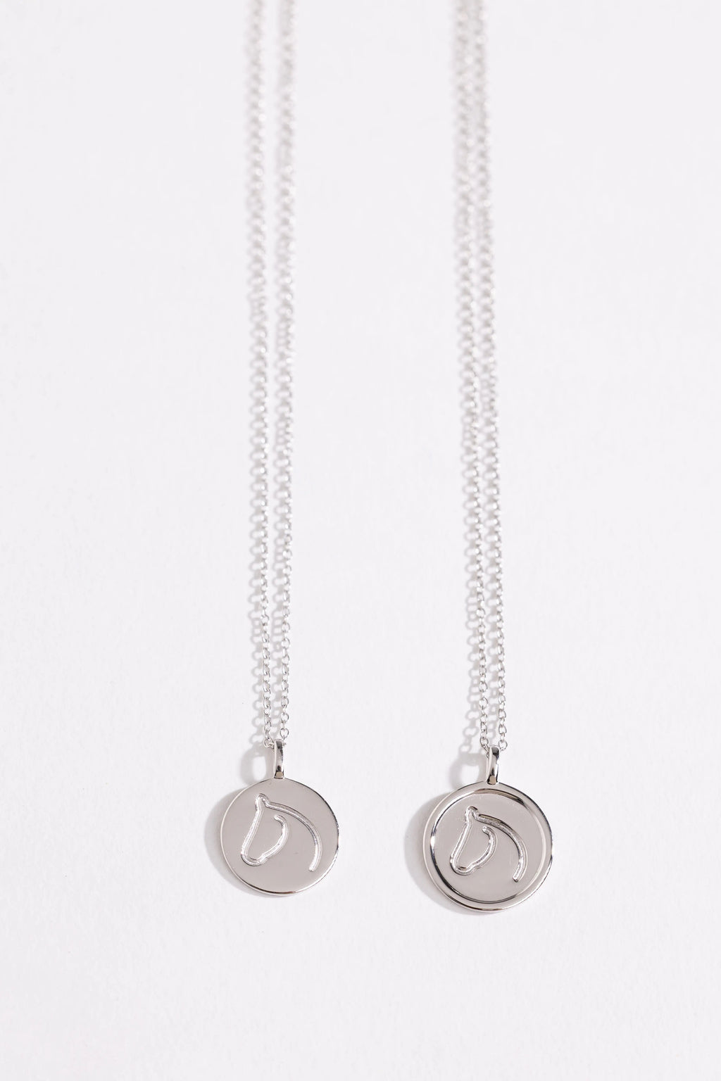 Two Sterling Silver necklaces from The Gilded Horse with round pendants on a white background.