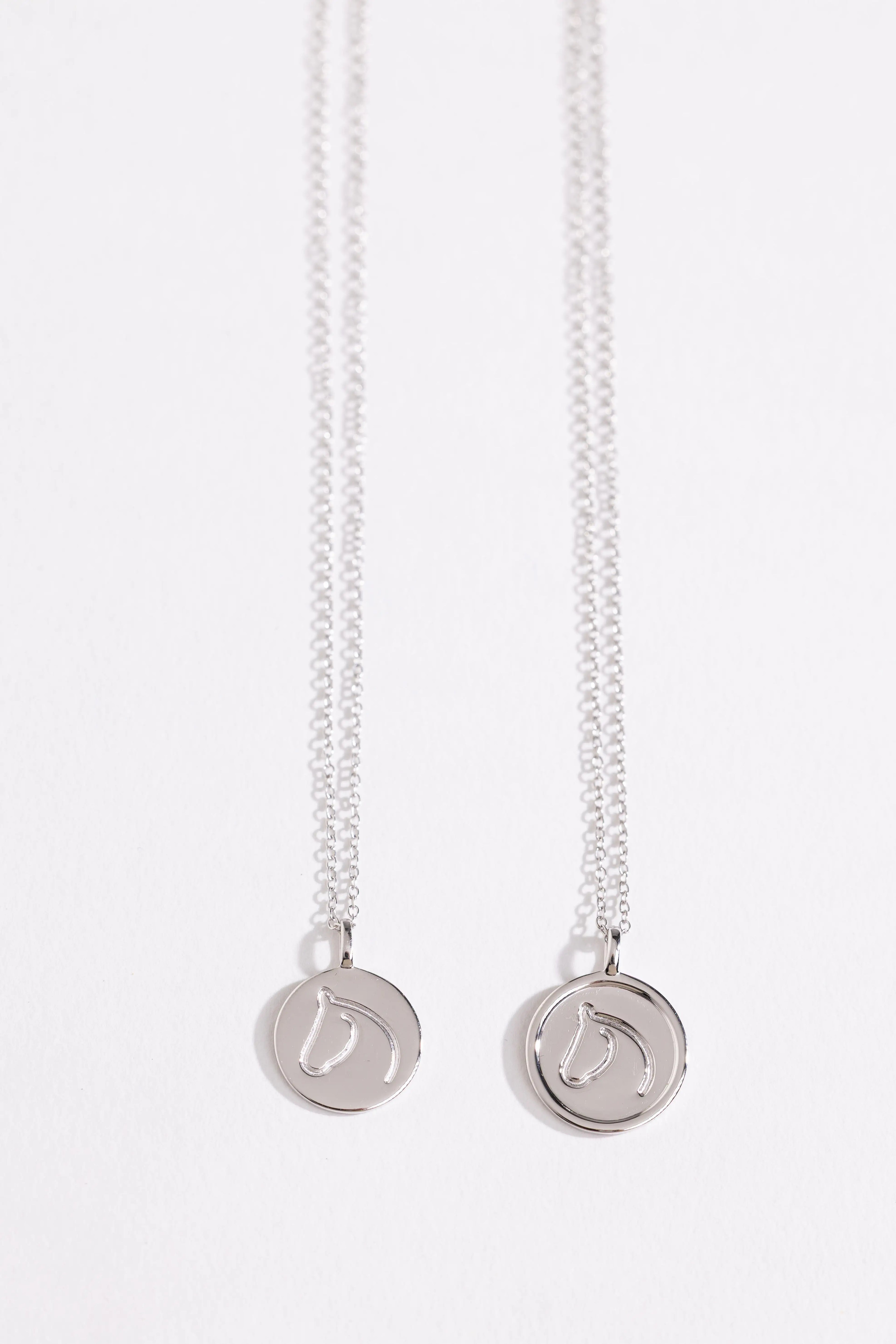 Two Sterling Silver necklaces from The Gilded Horse with round pendants on a white background.