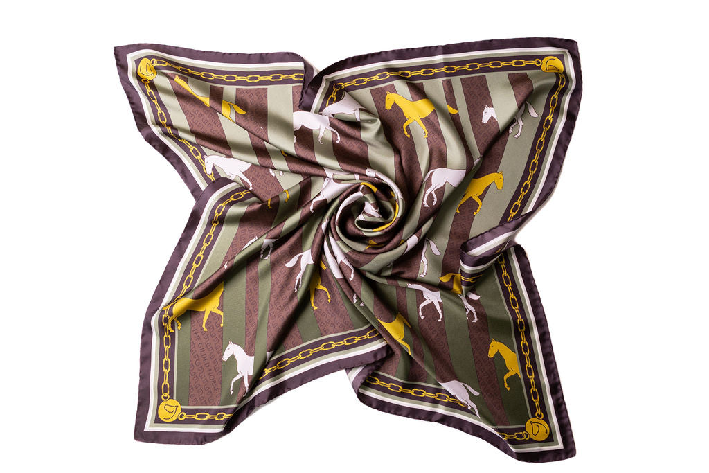 A square silk scarf with a twisted center, featuring a pattern of brown and olive green vertical stripes, white and yellow horse silhouettes, and a gold chain border on a white background.