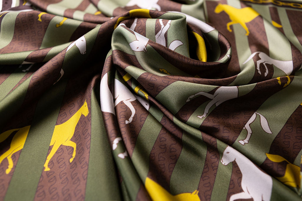 A close-up of draped fabric with a repeating pattern of brown vertical stripes, olive green bands, and white and yellow horse silhouettes.