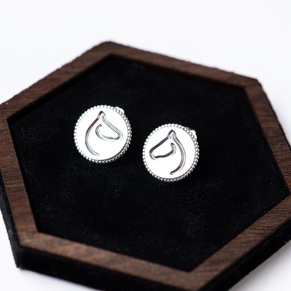 Pair of silver earrings on a black hexagonal stand with wooden border