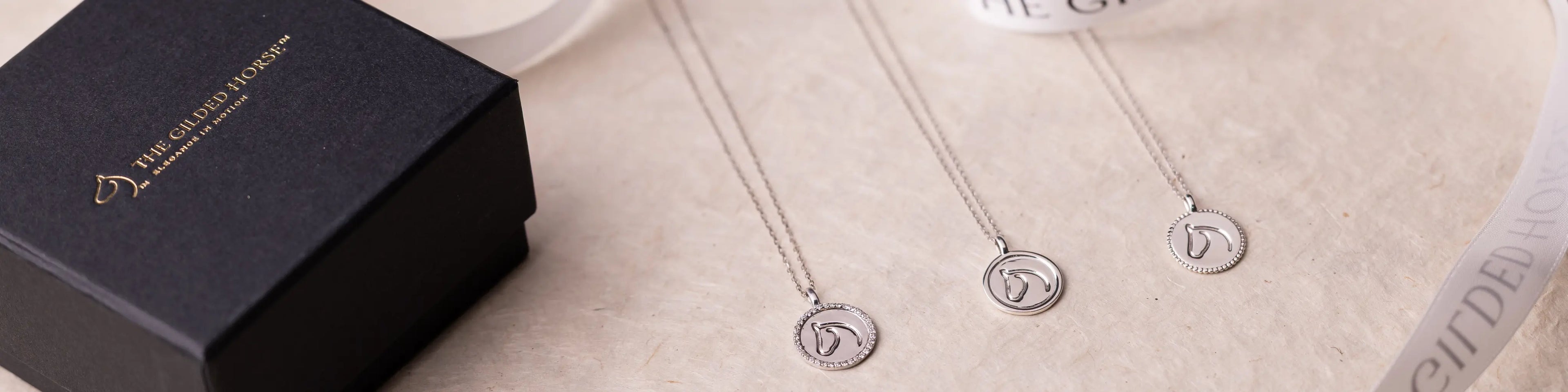 Three circle medallion horse necklaces with engraved horse-head, beside a black branded box