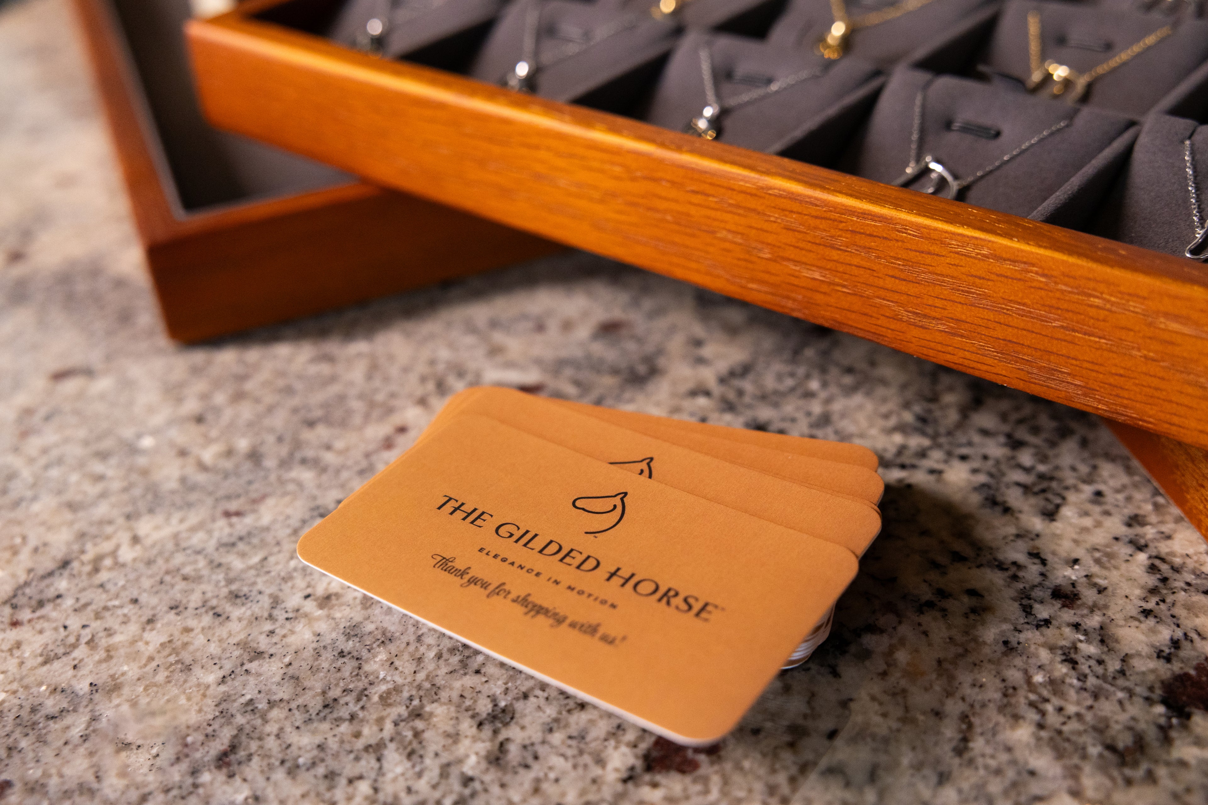 The Gilded Horse branded thank-you cards beside a wooden tray of necklaces
