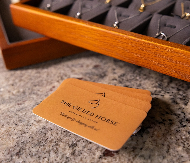 The Gilded Horse thank-you cards beside a tray of horse necklaces on a counter